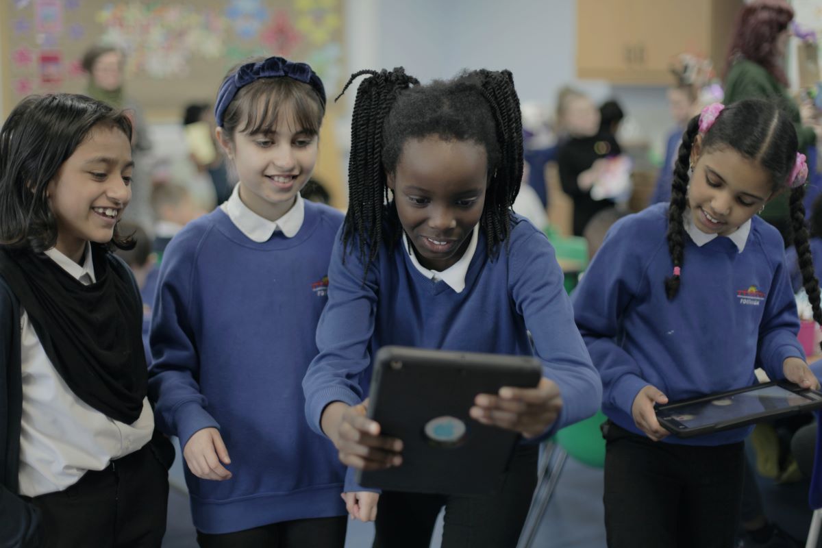 Children in school uniform working with an iPad together, looking on happily