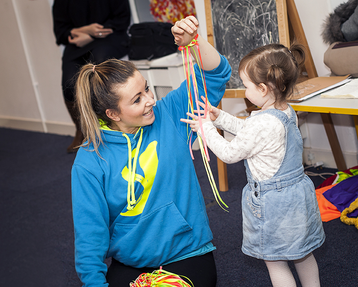 YDance activity Young child interacting with a dance worker who has coloured strings hanging from a wristband.